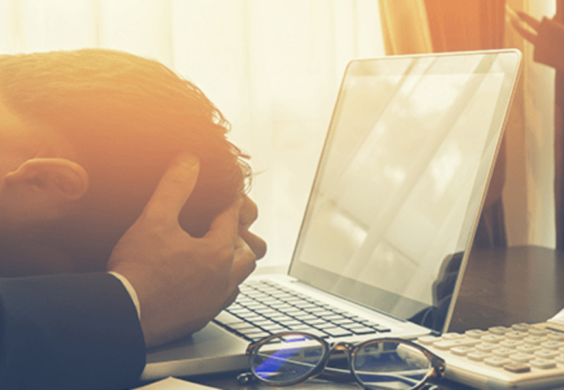 man with his head in hands laying on laptop