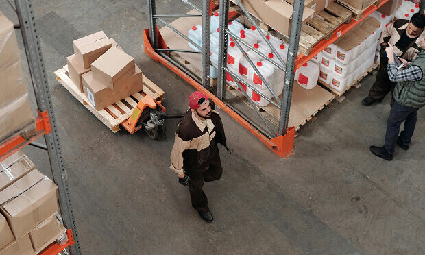 worker pulling crate and other workers inspecting products inside warehouse