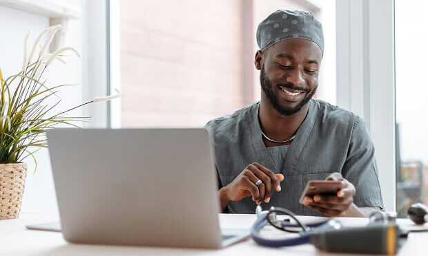man in doctor scrubs using phone and laptop