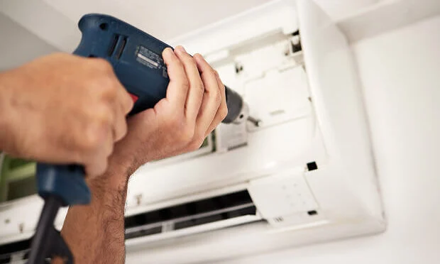 man drilling screw in AC unit